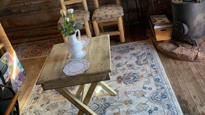 A cozy cabin interior with wooden walls, plaid curtains, a wooden table with a vase, a patterned rug, and a wood-burning stove. - Colorado Cabin with Hot tub, sauna, cold plunge! (Colorado)