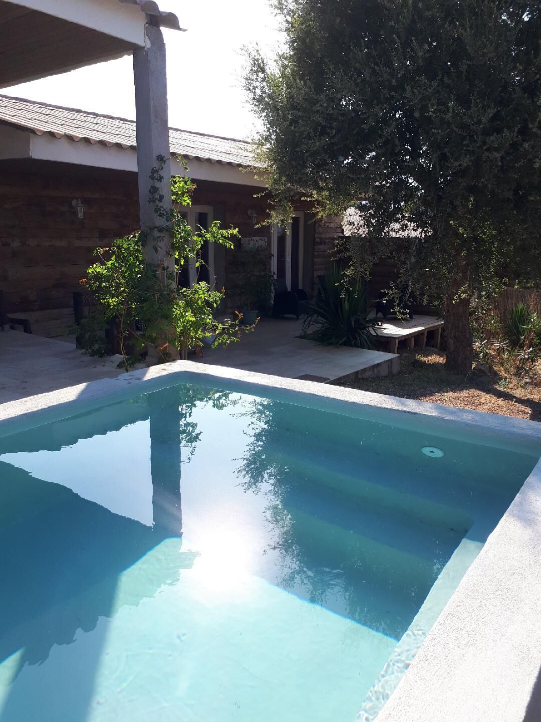 Een rechthoekig zwembad met helderblauw water, omringd door een betonnen terras en een stenen muur.