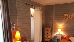 A bedroom with a bed, a nightstand, a lamp, a window with curtains, and a wooden wall.