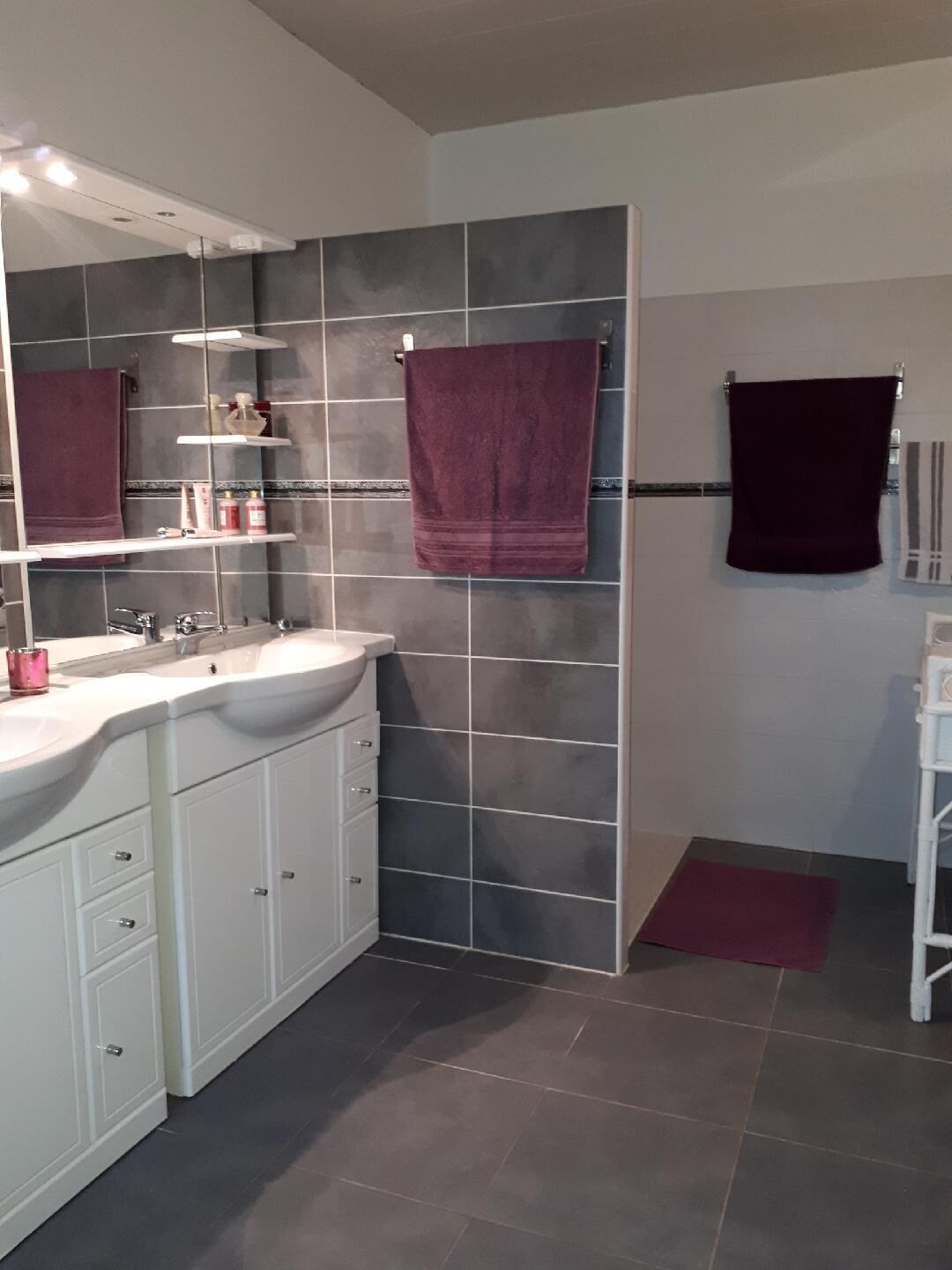 A modern bathroom with a large mirror, white cabinets, a marble countertop, and a dark tiled wall.