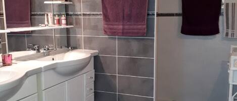 A modern bathroom with a large mirror, white cabinets, a marble countertop, and a dark tiled wall.