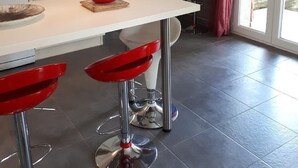 A modern kitchen with a white countertop, red bar stools, a microwave, and a coffee maker.