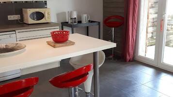 Une cuisine moderne avec un plan de travail blanc, des tabourets de bar rouges, un four à micro-ondes et une machine à café.