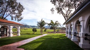 A building with a brick pathway leading to a green lawn, surrounded by trees and a clear sky. - La Lomita Ranch (San Luis Obispo)