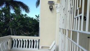 A balcony with white chairs, a white railing, and a door with a barred window. - Rose View Apartment Montego Bay (Montego Bay)
