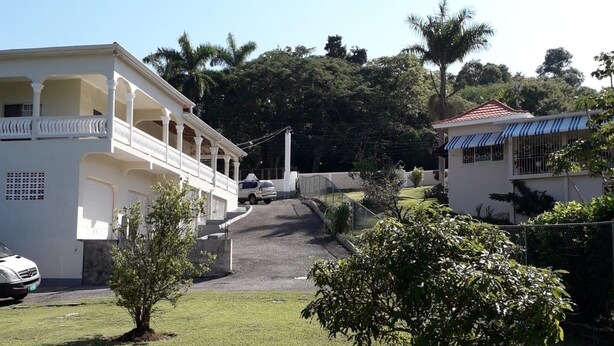 A white building with a balcony, a small tree in the foreground, and a car parked in front. - Rose View Apartment Montego Bay (Montego Bay)