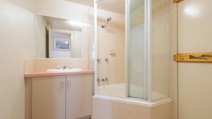 Une salle de bain avec une douche à parois de verre, un lavabo avec un miroir au-dessus et une étagère en bois ornée d’un objet décoratif.
