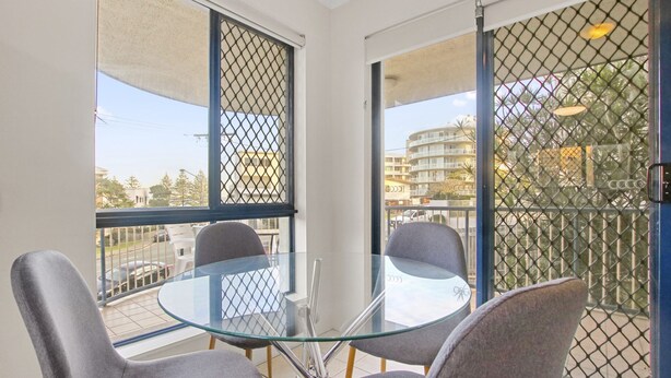 Un balcon avec une table et des chaises en verre, une vue sur le paysage urbain et une clôture en treillis métallique.