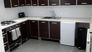 Una cocina moderna con armarios oscuros, encimera blanca, estufa, fregadero y lavavajillas.