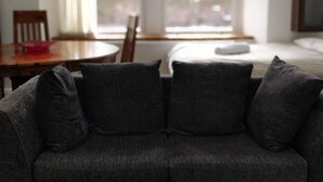 Una habitación con un sofá gris, una mesa de madera y una ventana con vistas a la vegetación.
