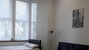 Un dormitorio con cama, sofá negro y lámpara de pie.