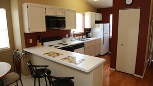 A compact kitchen with white cabinets, a microwave, stove, and refrigerator. There is a small dining area with two chairs and a table. - Top Floor Eagles Nest Condo with Pool and Hot Tub and Lake Views close to Silver (Branson)