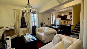 A spacious living room with a fireplace, white sofas, a dining area, and a kitchen in the background. - Daskios House , Skopelos Chora, a fully equipped house ideal for 2-3 guests (Skopelos)
