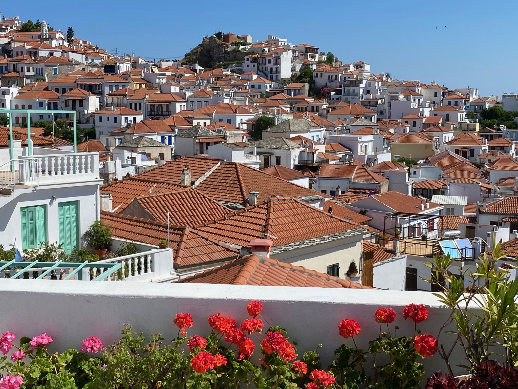 A densely packed hillside town with terracotta-tiled roofs, white buildings, and a prominent church with a bell tower.