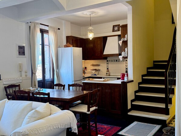 A compact kitchen with wooden cabinets, a white refrigerator, and a dining area with a table and chairs. - Daskios House , Skopelos Chora, a fully equipped house ideal for 2-3 guests (Skopelos)