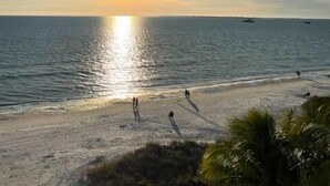 Une plage avec un ciel dégagé, le soleil se couchant ou se levant, et une mer calme.