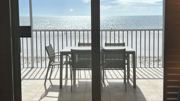 Un balcon avec une table et des chaises, donnant sur une plage et l’océan.