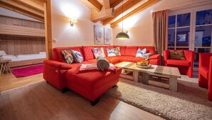 A cozy living room with a red sofa, wooden ceiling beams, and a large window with curtains. - Finest Penthouse All Seasons Lodge Kaprun (Kaprun)