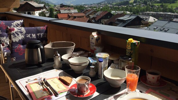 A balcony with a table set for breakfast, including a cup of coffee, a glass of orange juice, and a plate of food. - Finest Penthouse All Seasons Lodge Kaprun (Kaprun)