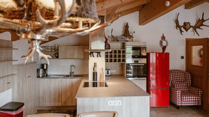 A modern kitchen with wooden cabinets, a central island, a red refrigerator, and a checkered chair. - Finest Penthouse All Seasons Lodge Kaprun (Kaprun)