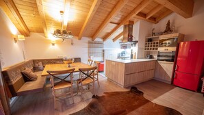 A cozy kitchen with wooden beams, a dining area with a wooden table and chairs, a red refrigerator, and a cowhide rug. - Finest Penthouse All Seasons Lodge Kaprun (Kaprun)