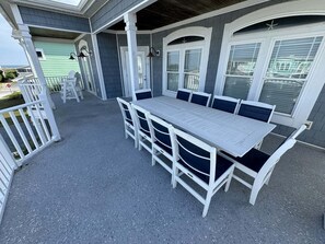 A covered patio with a white table and chairs, a railing, and a view of the ocean.