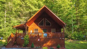 A wooden cabin with a porch, a staircase, and a sign indicating a rental price. - 🐾A Mountain Heart Song🔥Pet-Friendly, Fire Pit, Hot Tub & Gazebo (Sevierville)