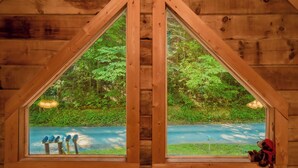 A wooden cabin with a triangular window revealing a forested area and a road. - 🐾A Mountain Heart Song🔥Pet-Friendly, Fire Pit, Hot Tub & Gazebo (Sevierville)