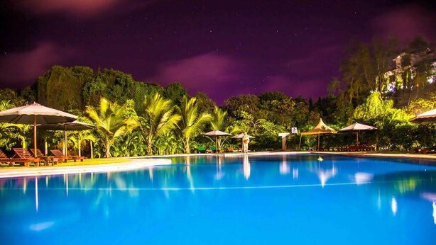 A nighttime pool area with umbrellas and lounge chairs. - Sunset Paradise Baringo 12 (Mombasa)