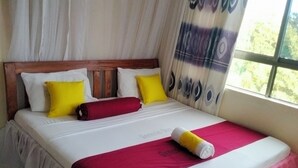 A bed with a wooden headboard, white bedding, and a pink skirt. - Sunset Paradise Baringo 12 (Mombasa)