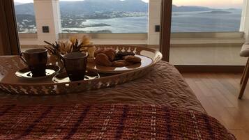 A bed with a tray of food and drinks, a view of mountains and water through large windows.