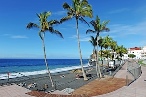 A beach with palm trees, a wooden deck, and a view of the ocean. - Apartamento Sabino en Puerto Naos (Puerto Naos)