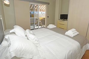 A hotel room with a large bed, a television on a dresser, and a sliding glass door leading to an outdoor area. - Apartamento Sabino en Puerto Naos (Puerto Naos)