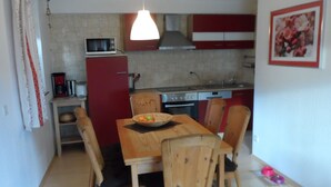 A compact kitchen with a microwave, stove, and red cabinets. There is a dining table with chairs and a bowl of fruit.