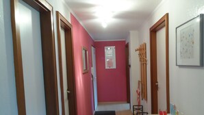A narrow hallway with pink walls, wooden doors, and a white counter with various items on it.
