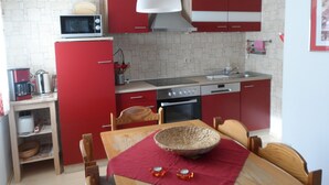 A compact kitchen with red cabinets, a microwave, a coffee maker, and a dining table with chairs.