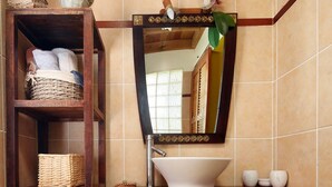 Een badkamer met een houten wastafelmeubel, een witte wastafel, een spiegel met decoratieve lijst en een geel vloerkleed.