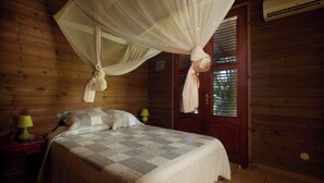 Een houten kamer met een bed, een nachtkastje, een lamp en een deur met een raam.