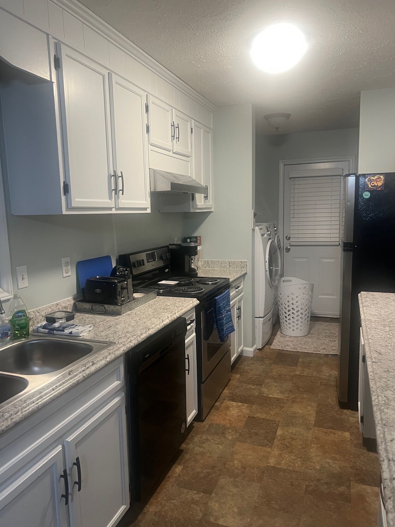 A compact kitchen with white cabinets, a black stove, a dishwasher, and a refrigerator.