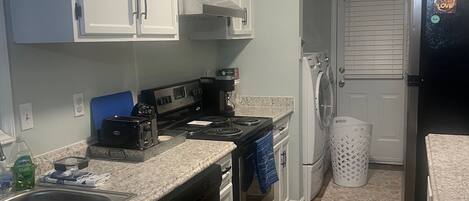 A compact kitchen with white cabinets, a black stove, a dishwasher, and a refrigerator.
