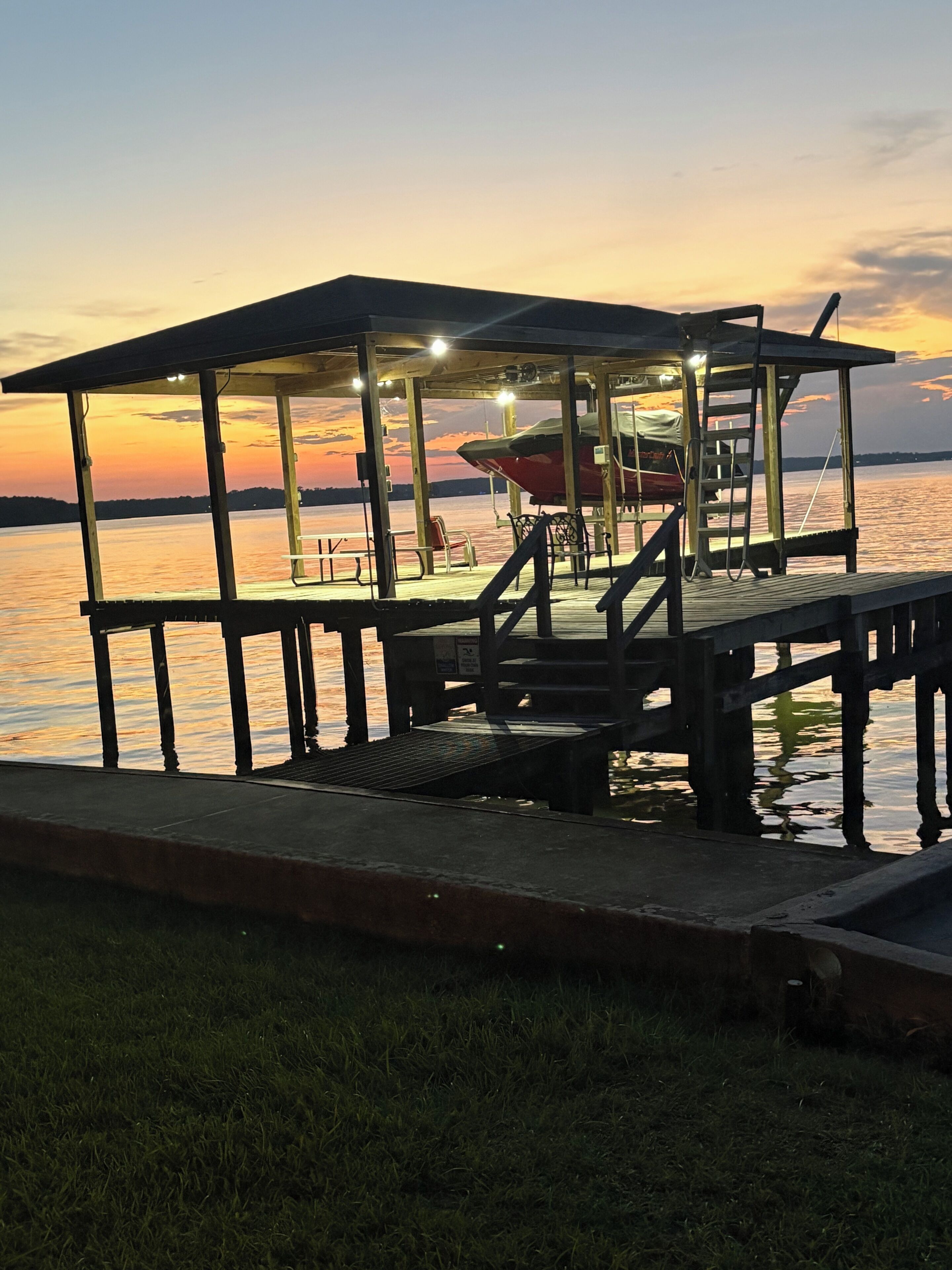 A wooden dock with a covered seating area overlooking a body of water during sunset.