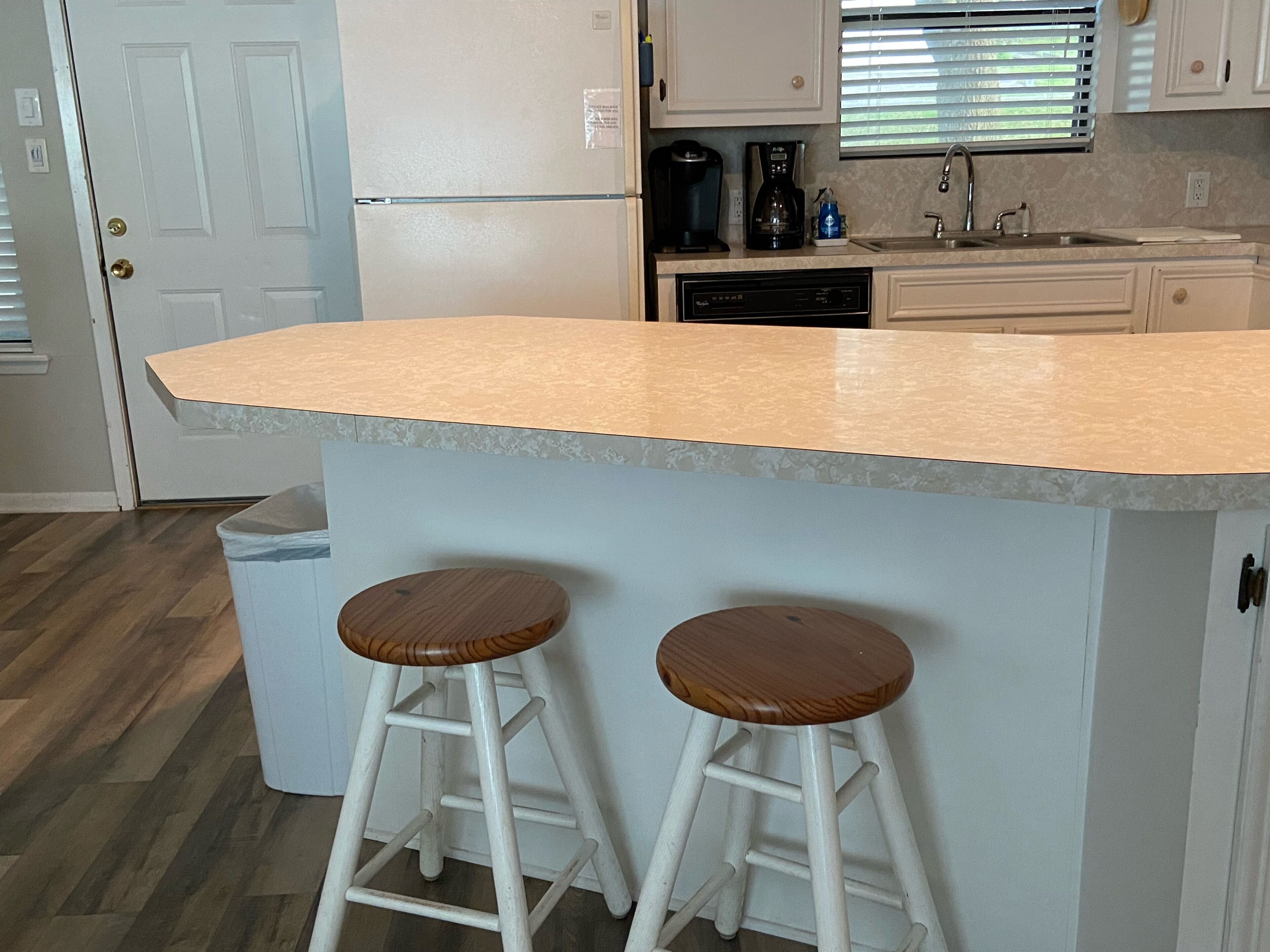A kitchen with a large island, two stools, a refrigerator, a coffee maker, and a sink.