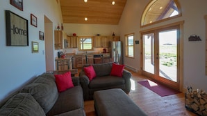 A spacious living area with a wooden ceiling, a kitchen with large windows, and a view of the outdoors. - Montana Prairie Cabin (McAllister)