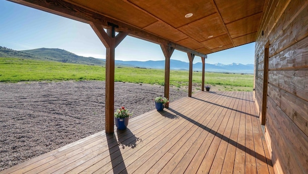 A wooden deck with a view of a green field and distant mountains. - Montana Prairie Cabin (McAllister)
