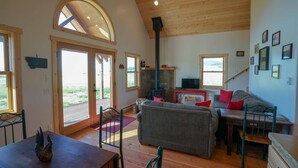 A cozy living room with a fireplace, a sofa, a dining table, and a staircase leading to another level. - Montana Prairie Cabin (McAllister)