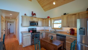A modern kitchen with wooden cabinets, stainless steel appliances, and a wooden dining table. - Montana Prairie Cabin (McAllister)