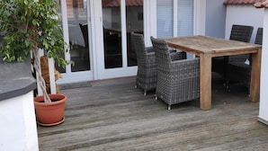 Eine Terrasse im Freien mit einem Holztisch, Korbstühlen, einem Blumentopf und einem Ziegeldach.