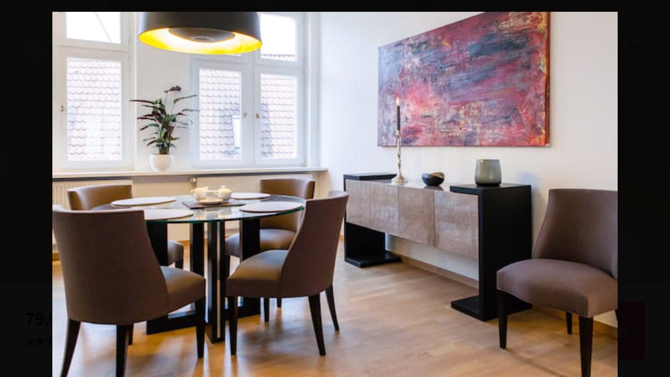 A modern dining area with a round table, six chairs, a potted plant, and a large abstract painting on the wall.