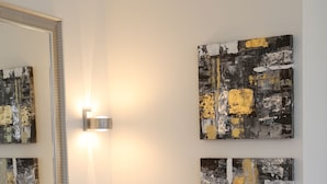 Ein Badezimmer mit schwarzem Waschtisch, einem Spiegel mit goldener Rahmung und zwei abstrakten Bildern an der Wand.