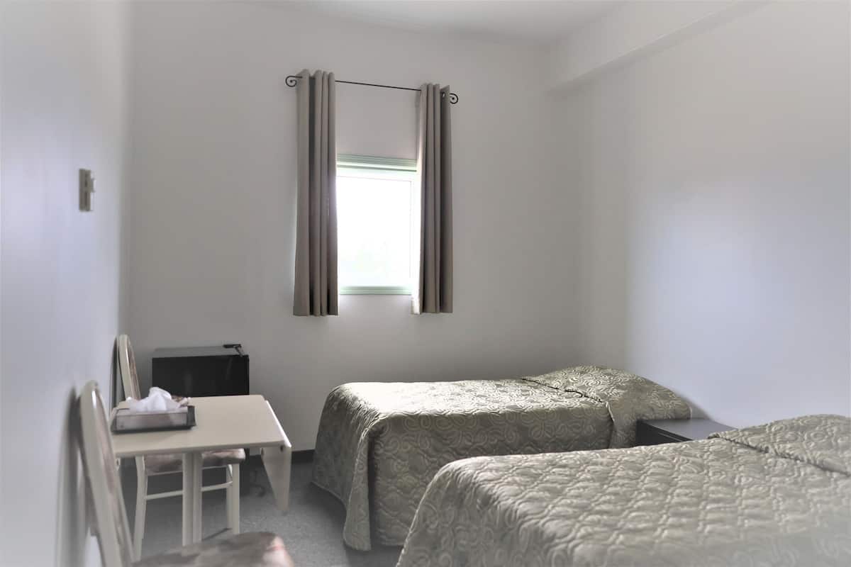 Una habitación sencilla con dos camas, un escritorio y una silla.